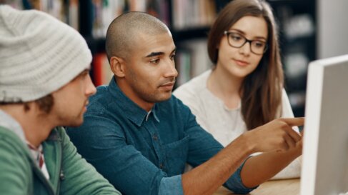 Group of college students look at a computer monitor in a college library